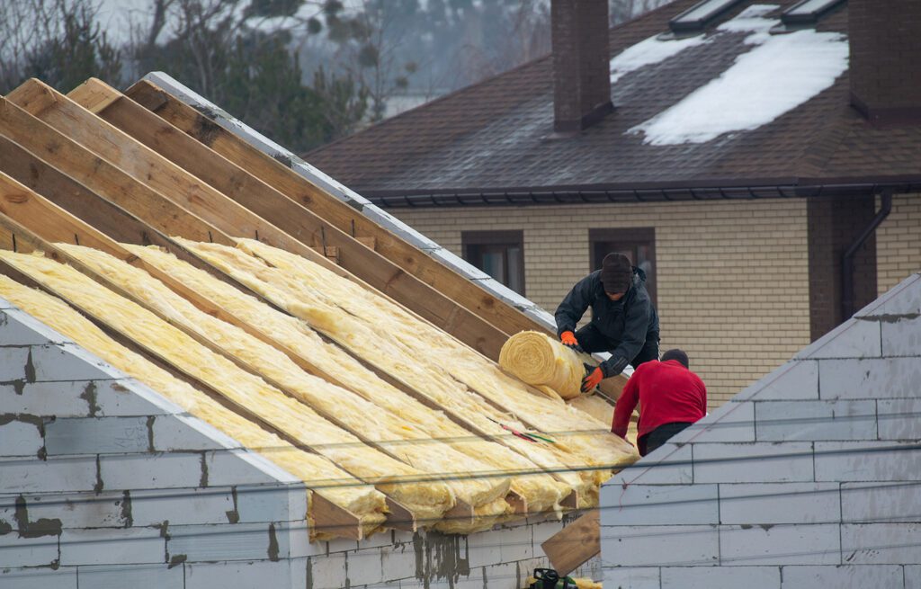 Roofer builder worker installing roof insulation material on a house roof